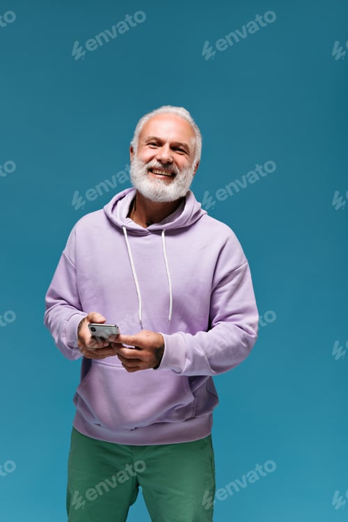 Preview: Cool man wearing hoodie and shorts smiles and holds phone. Handsome guy with white beard in lilac s