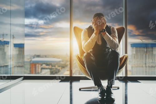 Preview: A businessman on an armchair covering his face with his hands, stormy sky behind