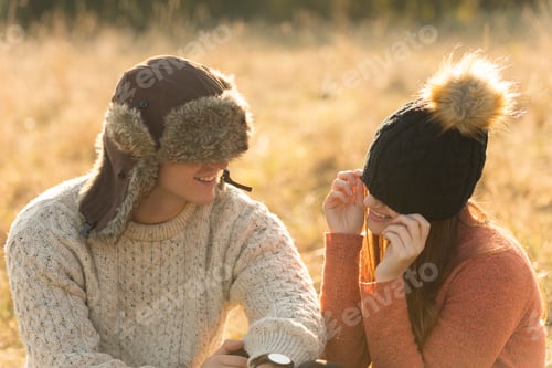 Preview: Young couple sitting in rural setting, wearing warm hats