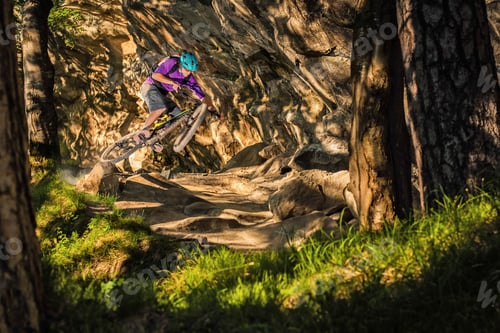 Preview: Young male mountain biker jumping over rock formation in forest