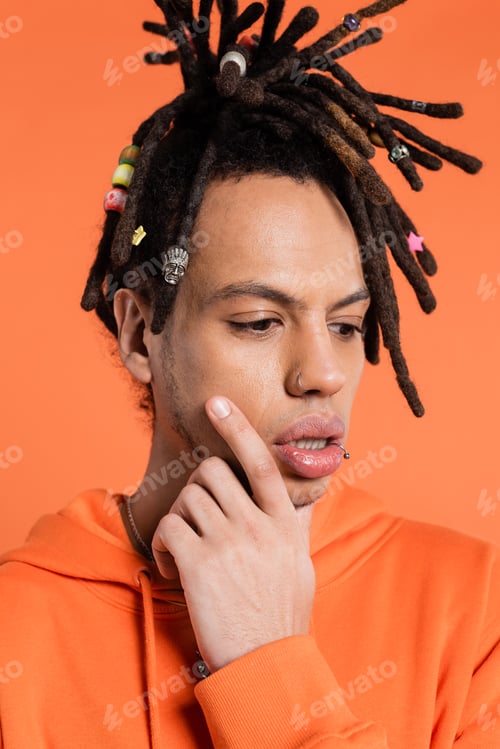Preview: portrait of multiracial man with dreadlocks touching face while thinking isolated on coral