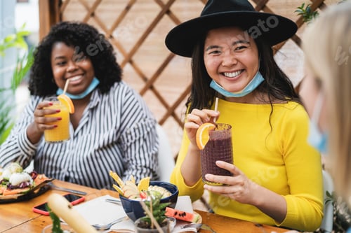 Preview: Multiracial friends having healthy lunch drinking fruits fresh smoothies in coffee brunch bar