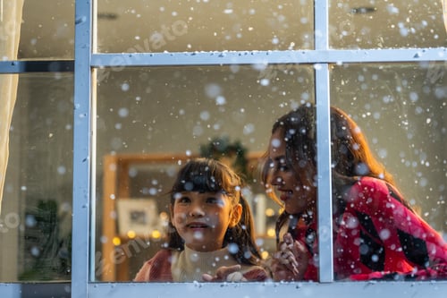 Preview: Adorable child looking at the window and admire snowflakes with mother.