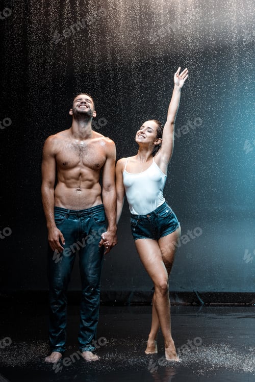 Preview: happy couple standing and holding hands under raindrops on black