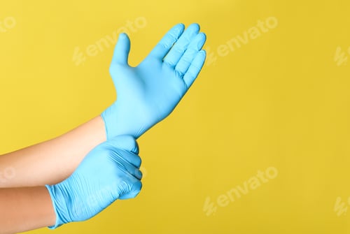 Preview: Person putting on blue latex gloves against yellow background, closeup. Space for text
