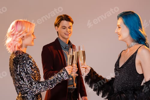 Preview: smiling and elegant queer friends clinking champagne glasses during christmas party on grey