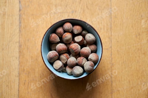 Preview: Top view of a bowl of hazelnuts on a wooden table in a blurred background