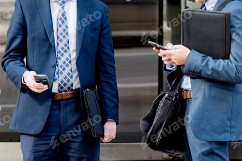 Preview: Businessmen wearing suits using smart phone devices holding travel briefcases
