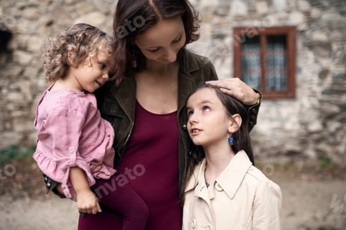 Preview: A mother with two small daughters standing in front of old stone house