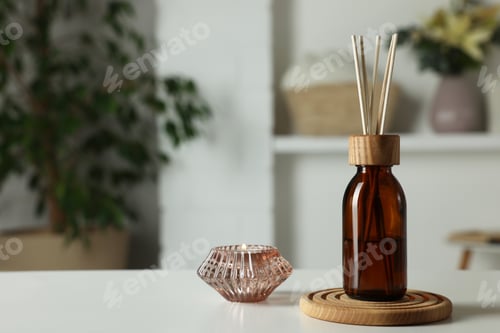 Preview: Aromatic reed air freshener and candle on white table in room. Space for text