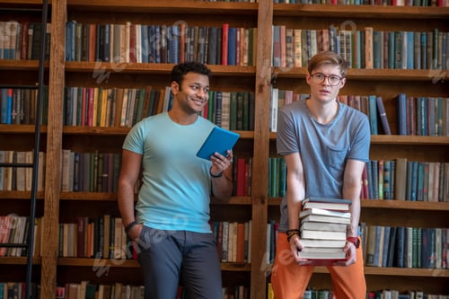Preview: Two young men standing in the library holding books