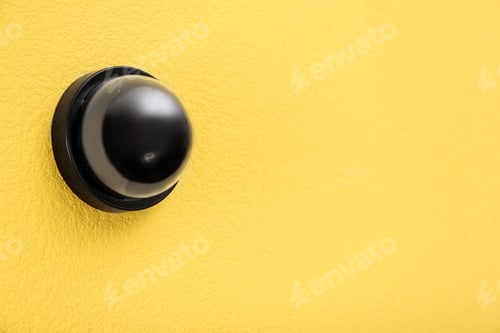 Preview: Modern CCTV security camera on yellow wall. Space for text