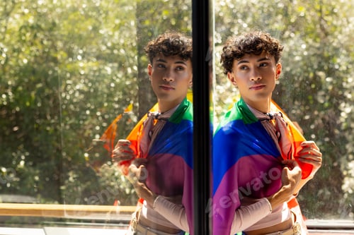 Preview: Holding rainbow flag, transgender woman standing by window with reflection in glass