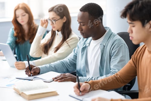 Preview: Diverse Students Sitting At Desk In Line Taking Notes