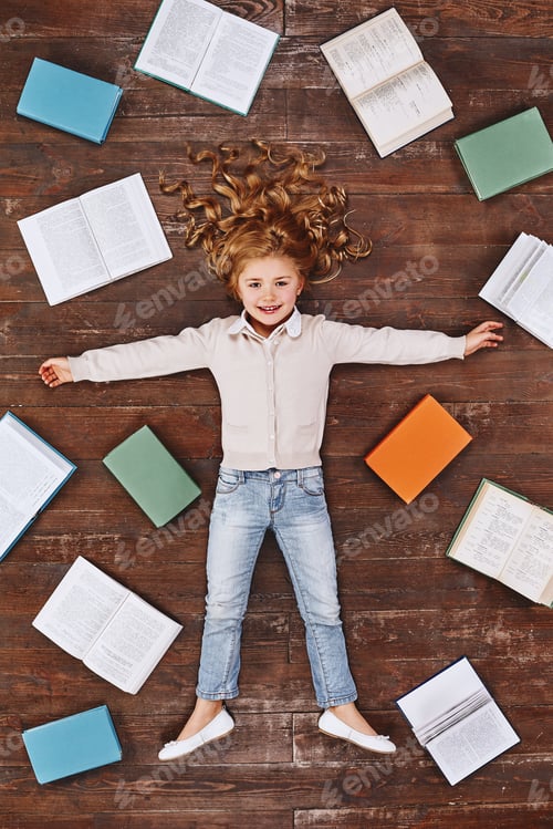 Preview: Time for dreaming. Girl lying near books, looking at camera and smiling