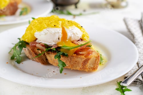 Preview: Sandwich with ham, poached egg, onion and arugula in a plate on a light background