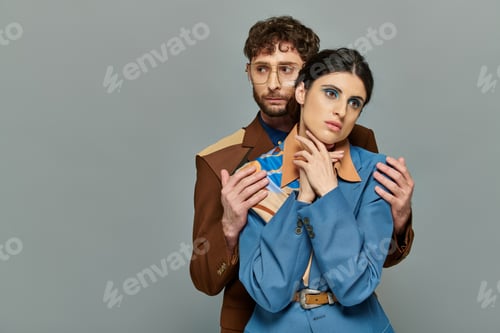 Preview: bearded man in glasses hugging pretty woman, fashion models, trendy suits, grey background, elegant