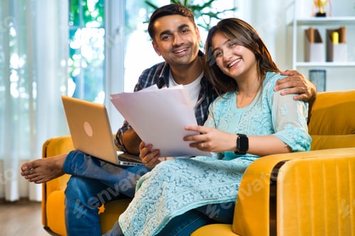 Preview: Indian Asian couple happily budgeting and working on finances with laptop and documents at home