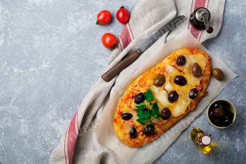 Preview: Oval pizza Greek with olives and with tomato on gray concrete background. Selective focus. Top view.
