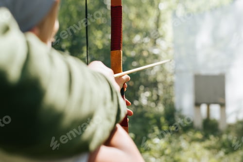 Preview: Close-up of child learning medieval archery outdoors. Back view, selective focus on wooden weapons