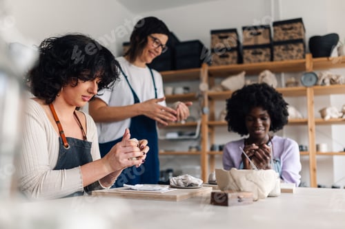 Preview: Interracial pottery class students modeling clay with tutor at studio.