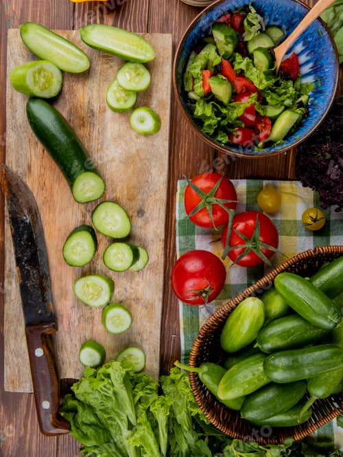 Preview: top view of cut and sliced cucumber with knife on cutting board with vegetable salad, tomatoes