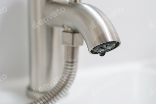 Preview: Drop of water flows from a tap in a bathroom on light background.