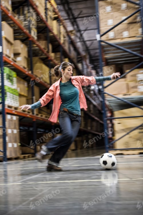 Preview: A caucasian female aboiut to kick a soccer ball during a work break in a distribution warehouse.