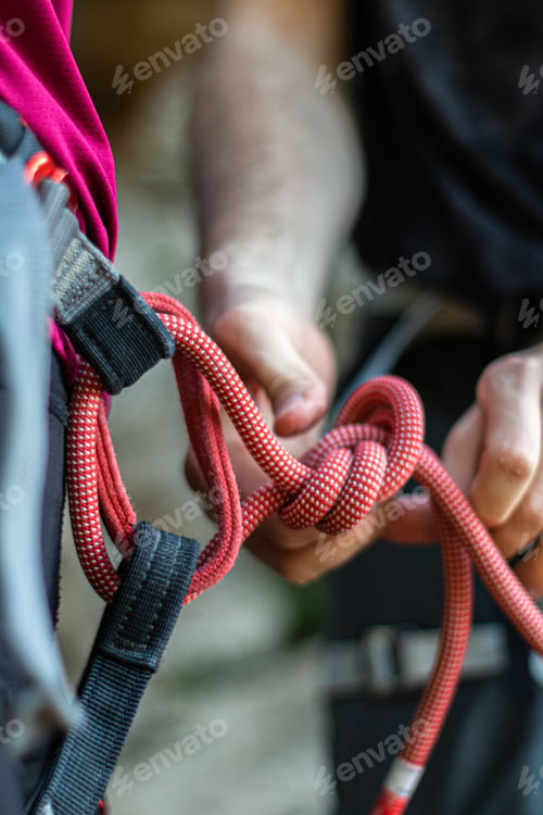 Preview: Alpinist tying a rope on his climbing equipment