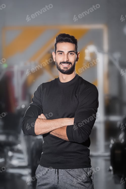 Preview: Young arabian sportsman smiling at camera in blurred gym