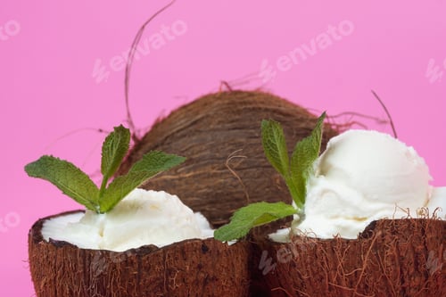 Preview: Vanilla ice cream balls in fresh coconut halves decorated with mint leaves on a pink background