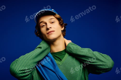 Preview: Young man showcases trendy fashion against a vibrant blue background bringing modern style to life