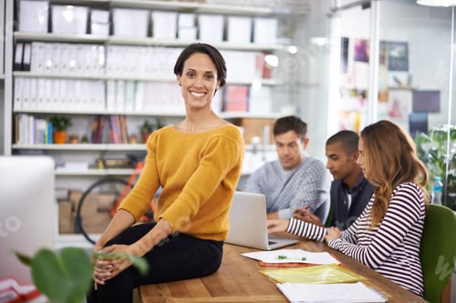 Preview: A young designer smiling while her team has a meeting in the background