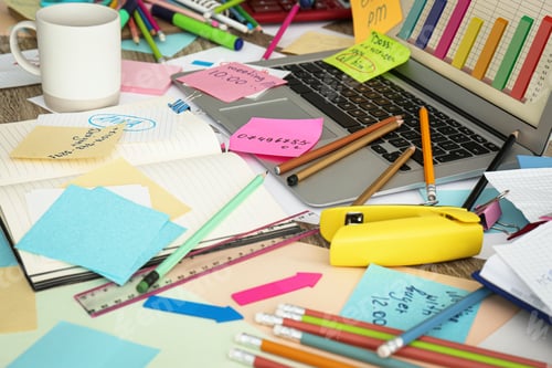 Preview: Laptop, notes and office stationery in mess on desk. Overwhelmed with work