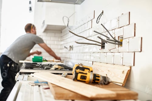 Preview: A man working in a new kitchen, a tiler applying tiles to the wall behind the cooker.