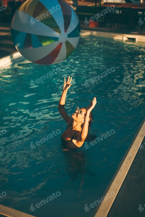Preview: Young woman with ball in the pool at sunny day