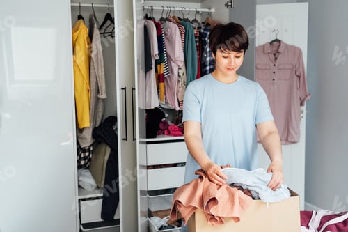 Preview: Woman selecting clothes from her wardrobe for donating to a Charity shop. Decluttering, Sorting