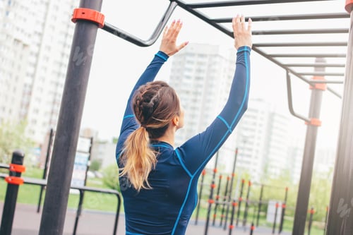 Preview: Attractive fit young woman in sport wear girl pulls up on bar at street workout area