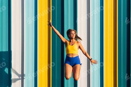 Preview: Young woman jumping in front of colorful wall