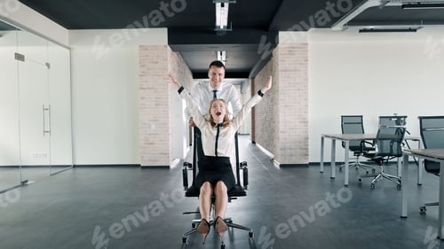 Preview: Male employee pushing his female coworker on a roller chair, having silly fun at the office