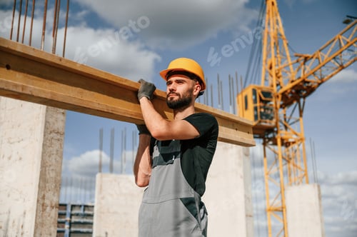 Preview: Holding and walking with wooden plank. Man in uniform is working on the construction site