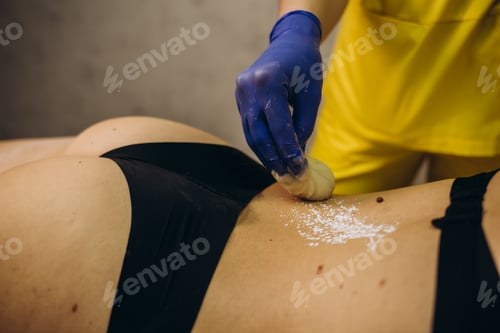 Preview: Mid section of therapist waxing womans back at spa center