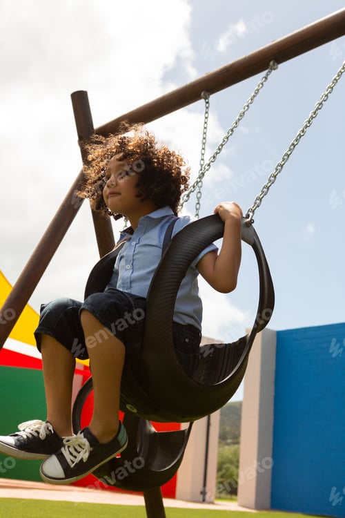 Preview: Schoolgirl playing in a swing swing in the school playground on a sunny day