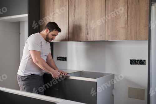 Preview: Young latin man using measuring tape before placing countertops on kitchen.