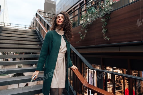 Preview: Portrait of young woman in green coat with curly hair in the city