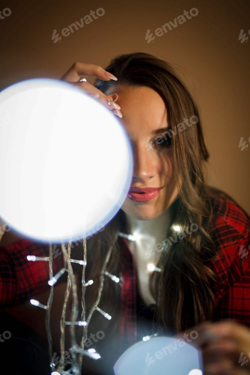 Preview: Portrait of a Bosnian sexy girl holding Christmas lights next to a lamp and looking at the camera