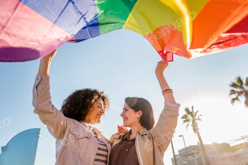 Preview: smiling young lesbian couple waves a rainbow flag