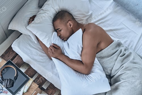 Preview: Lazy morning. Top view of young African man sleeping while lying in the bed at home