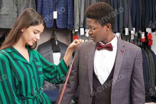 Preview: Consultant measuresing jacket sleeve on client in boutique