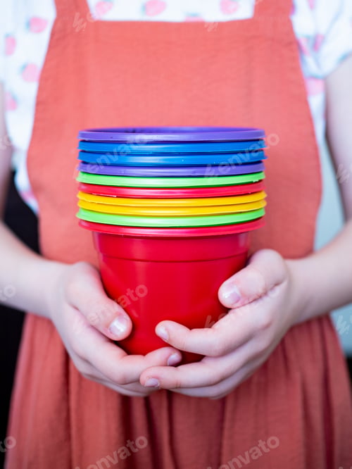 Preview: young girl in an apron holds bright colorful pots for planting in her hands